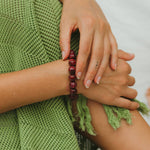 Close-up of hands with a red beaded bracelet, wearing a green knitted garment.