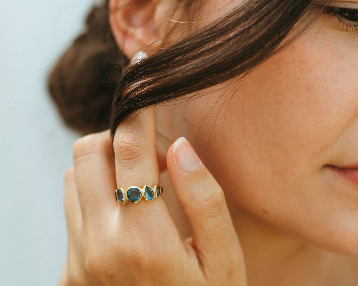Close-up of a woman wearing a blue ring and earring, with a blurred background