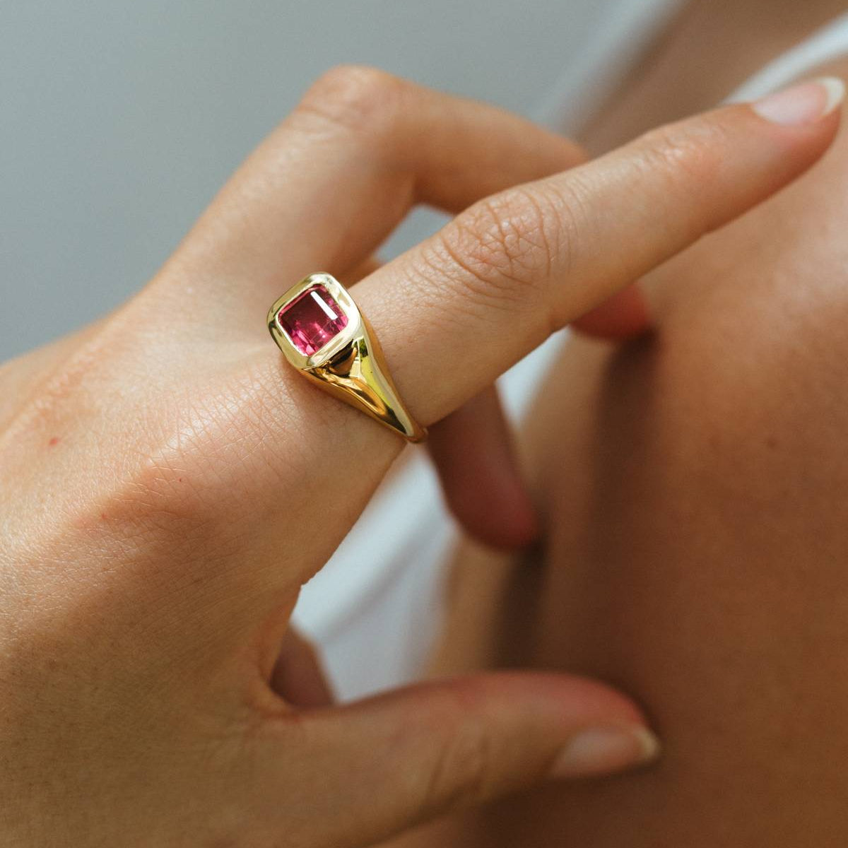 Gold ring with a pink gemstone on a finger against a neutral background