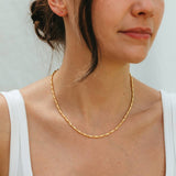 Woman wearing a gold necklace against a plain background