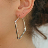 Close-up of a person wearing a silver geometric hoop earring.