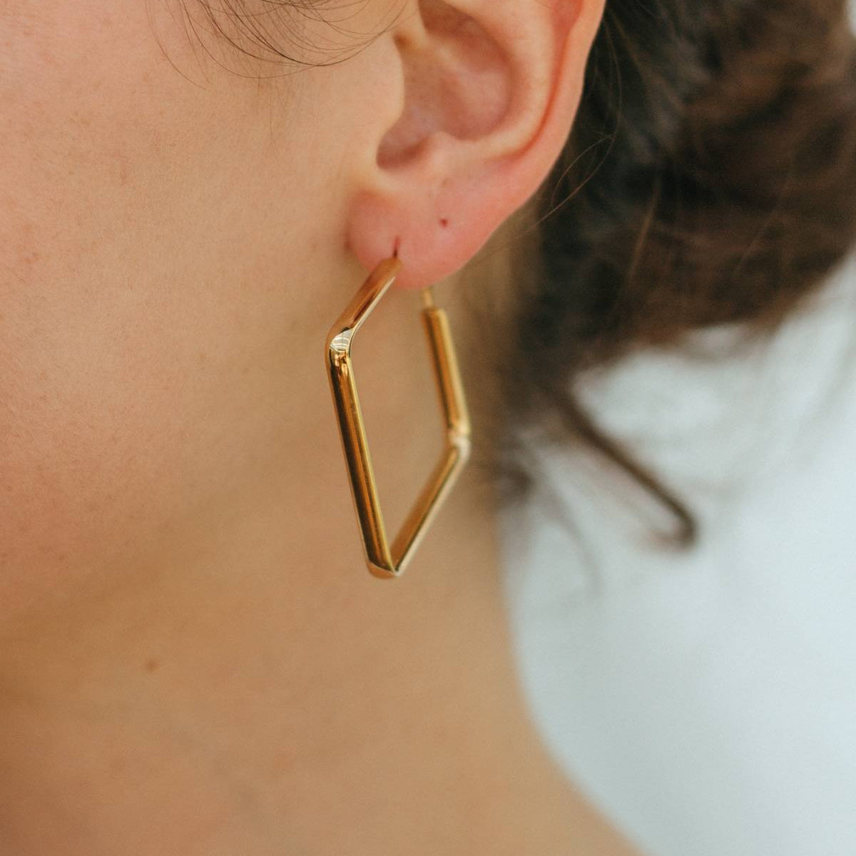 Gold geometric hoop earring worn by a person with a blurred background