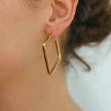 Gold geometric hoop earring worn by a person with a blurred background
