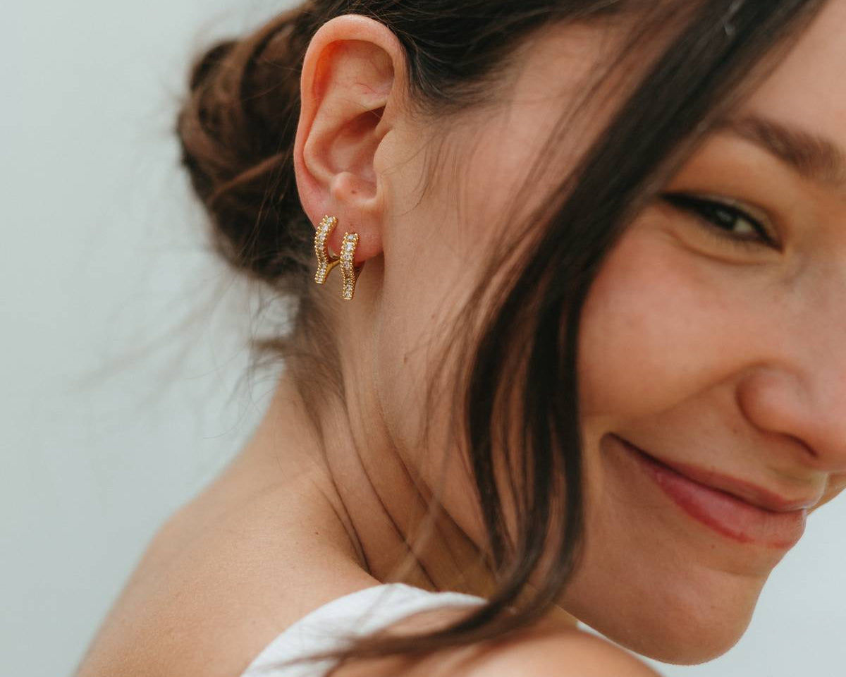 Woman with a side bun wearing gold earrings against a light background