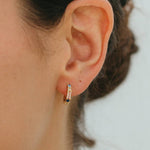 Close-up of an ear wearing a small hoop earring with a neutral background