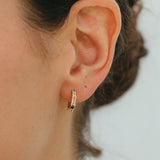 Close-up of an ear wearing a small hoop earring with a neutral background