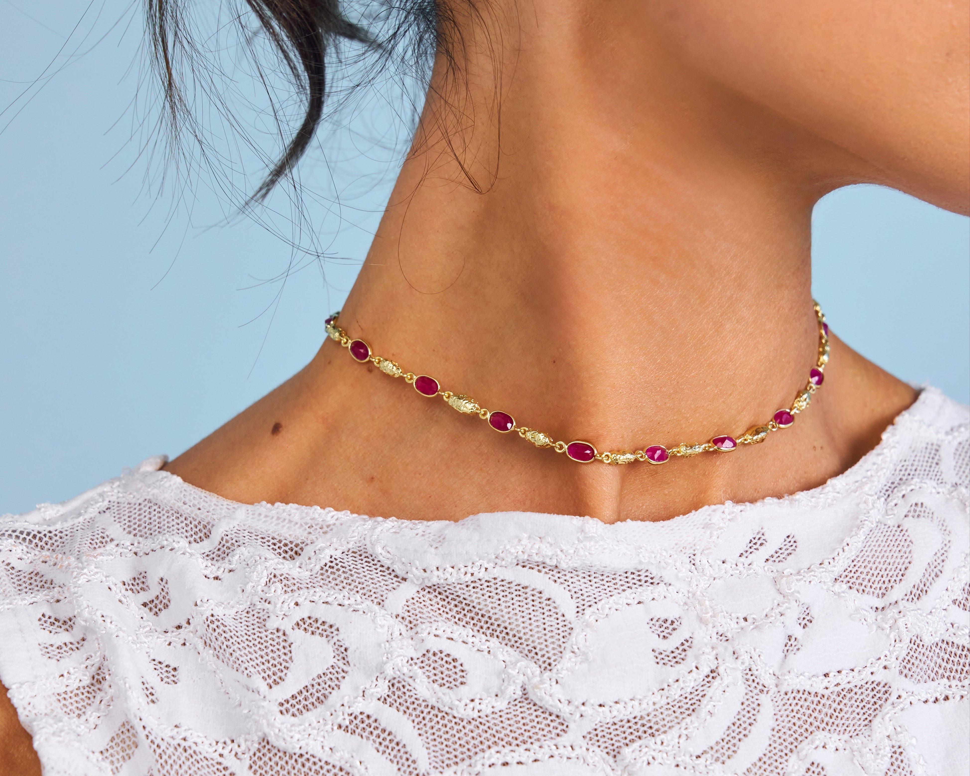 Close-up of a woman wearing gold earrings and a necklace with a blue background